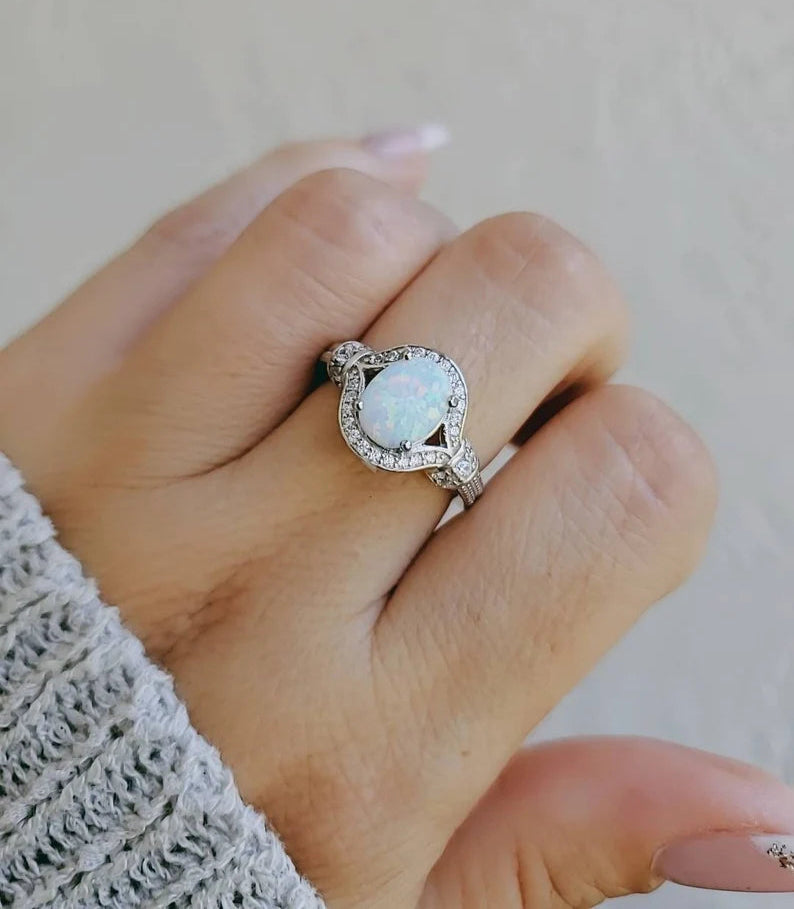 A sterling silver ring with a central lab-created opal surrounded by clear cubic zirconia stones, displayed on a person's hand.